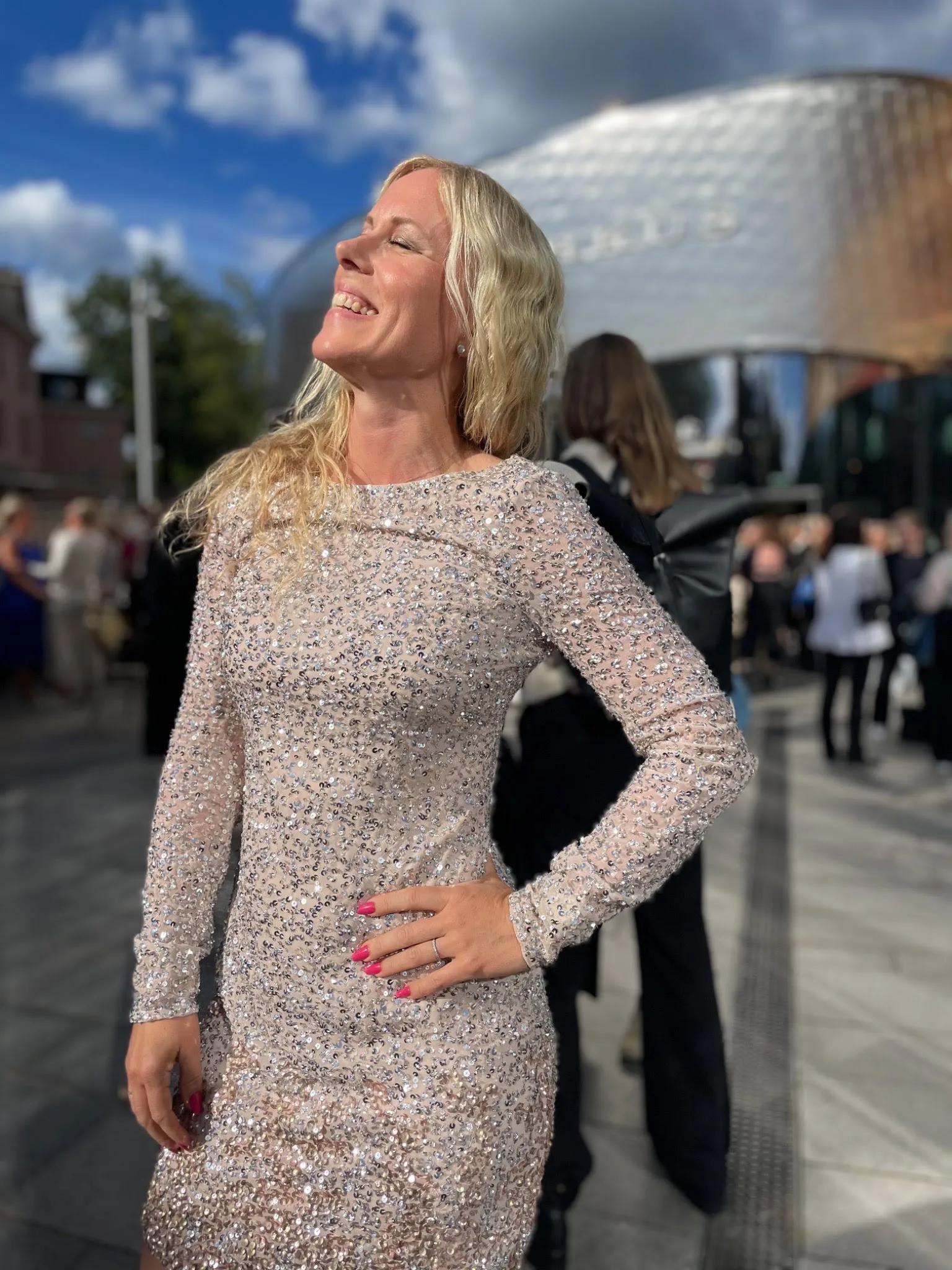 Ann-Sofie skrattar i en glittrande klänning utomhus.